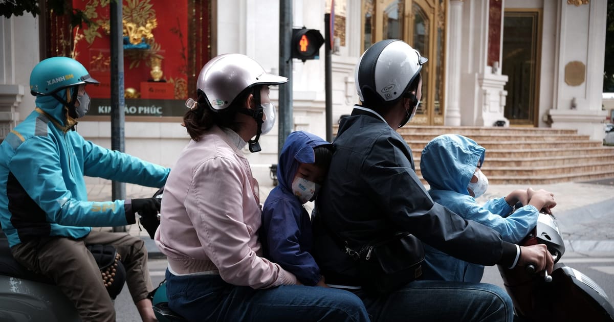 A family riding together on a scooter in city traffic.