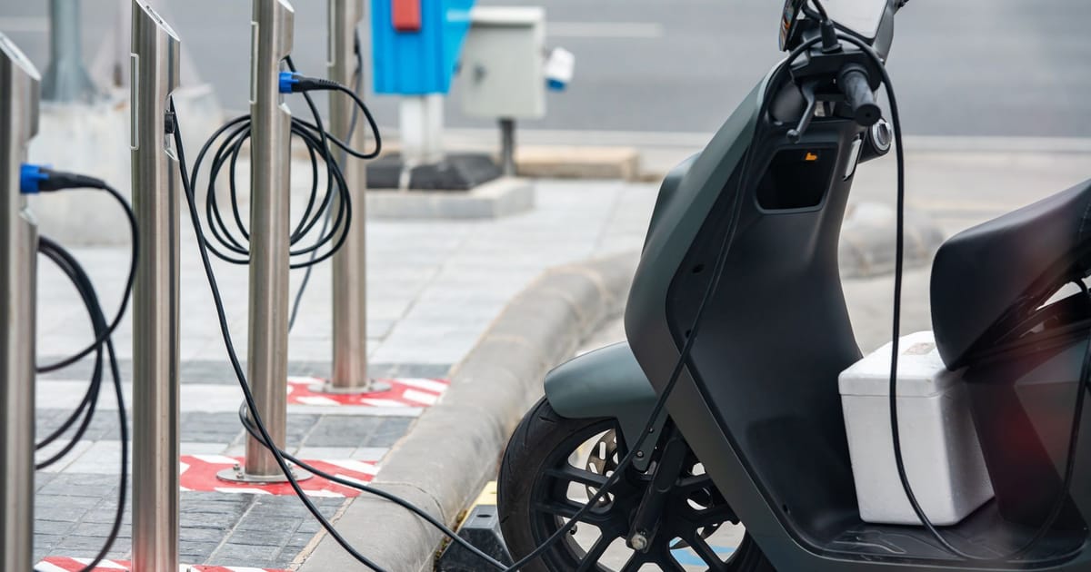 An electric scooter plugged in at a public charging point.