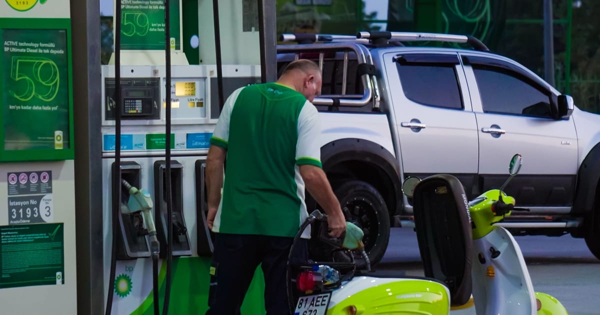 A forecourt attendant refuelling a scooter.